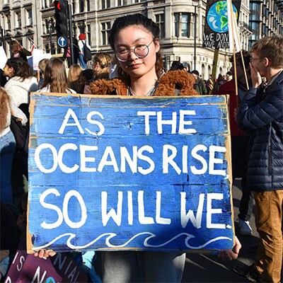 Protester holding a sign that reads ‘As the oceans rise so will we’